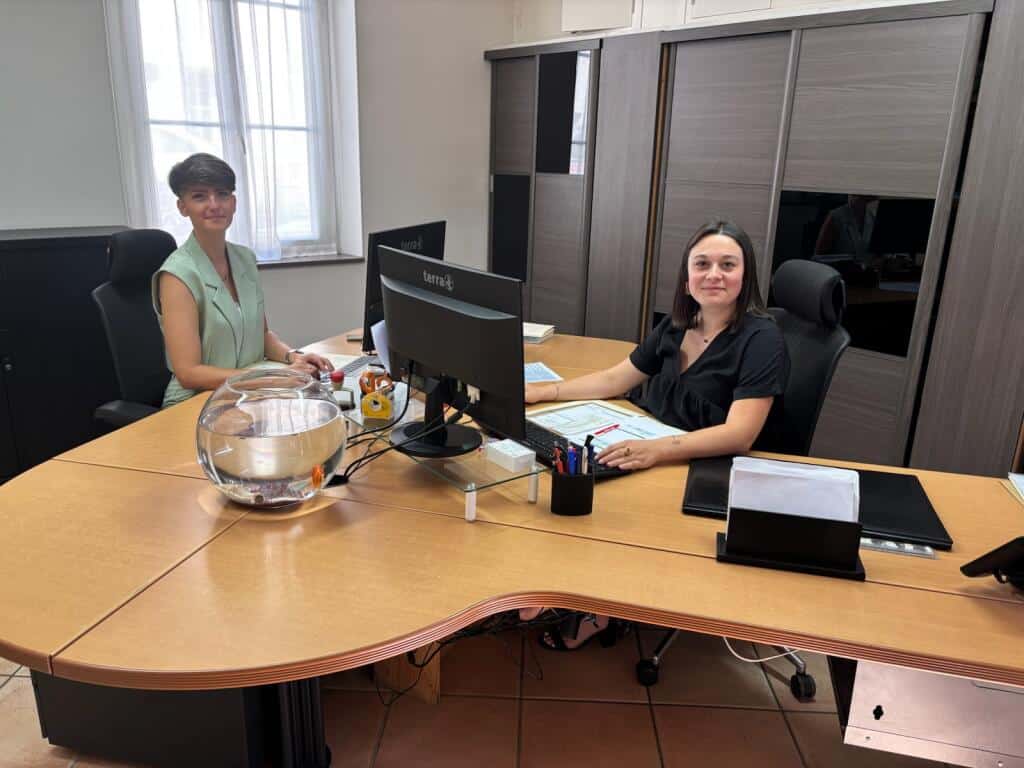 Deux employées souriantes à un bureau d'accueil avec écrans Terra et bocal à poisson.