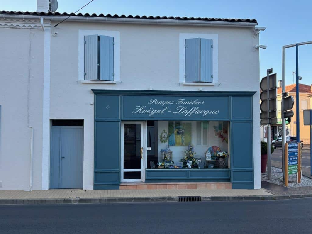 Façade des Pompes Funèbres Koëgel-Laffargue, bâtiment blanc à devanture bleue et vitrine fleurie.